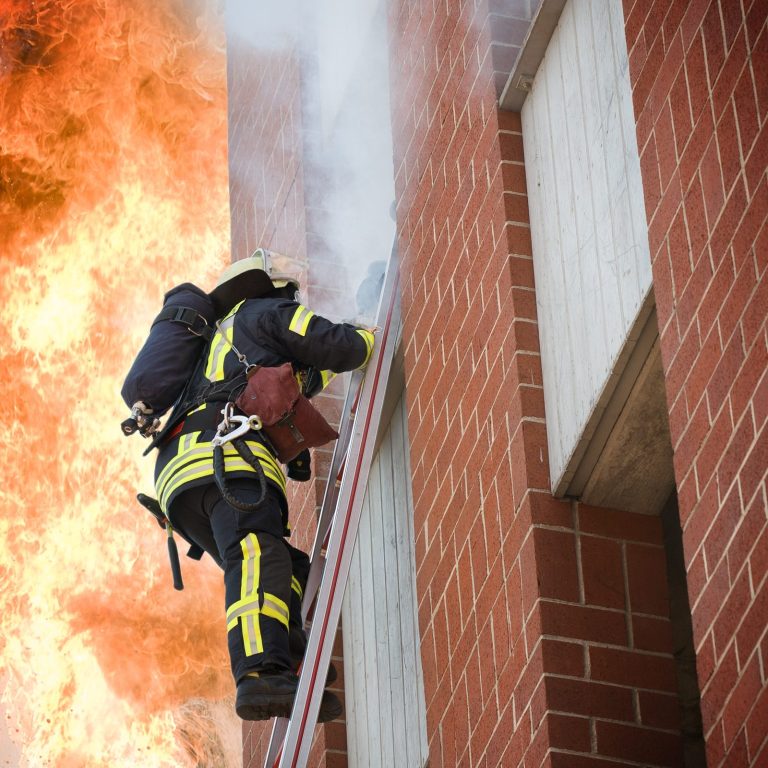 Ein Feuerwehrmann auf einer Leiter an einem brennenden Gebäude